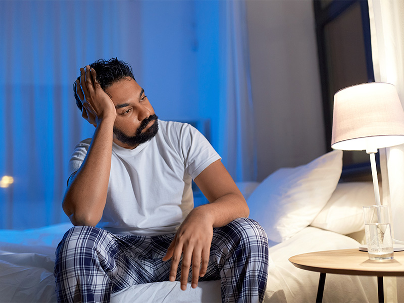 Mann sitzt nachts im Bett und leidet an Schlafproblemen, wirkt gestresst und wach, Symbol für Schlafprobleme in Herdecke.