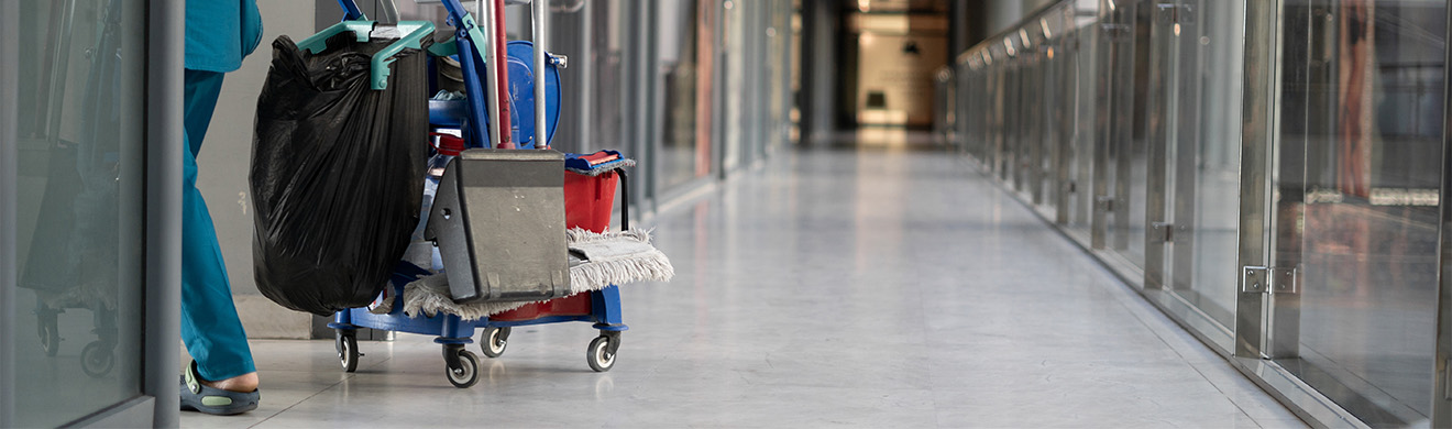 Frau bei der Gebäudereinigung in Hagen zieht Putzwagen durch Büroflur und sorgt für Sauberkeit am Arbeitsplatz.