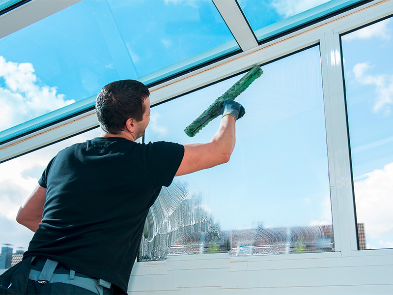 Fachkraft führt sorgfältige Glasreinigung an großen Fenstern durch und sorgt für streifenfreie Sauberkeit und klare Sicht.