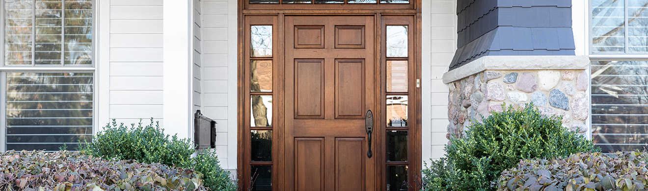 Elegante, individuelle Holztür in Hagen, umgeben von Fenstern und moderner Hausfassade aus Stein, Holz und Farbelementen.