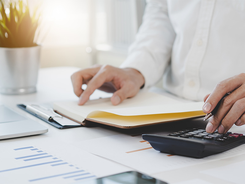 Ein Wirtschaftsprüfer in Hagen prüft sorgfältig Belege und berechnet Finanzdaten mit einem Taschenrechner an einem ordentlich strukturierten Arbeitsplatz.